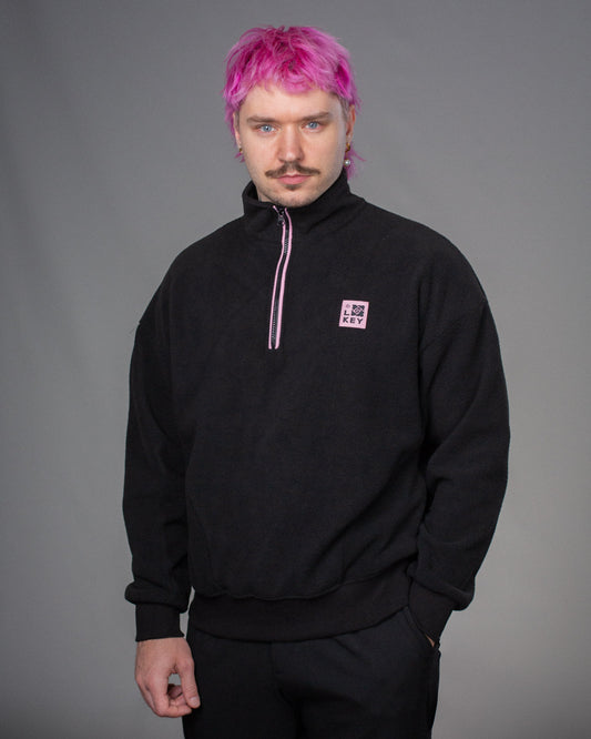 Schwarzer Fleece-Troyer mit halbem Reißverschluss und kleinem rosa Logopatch mit „LOKEY“-Schriftzug auf der linken Brust.
