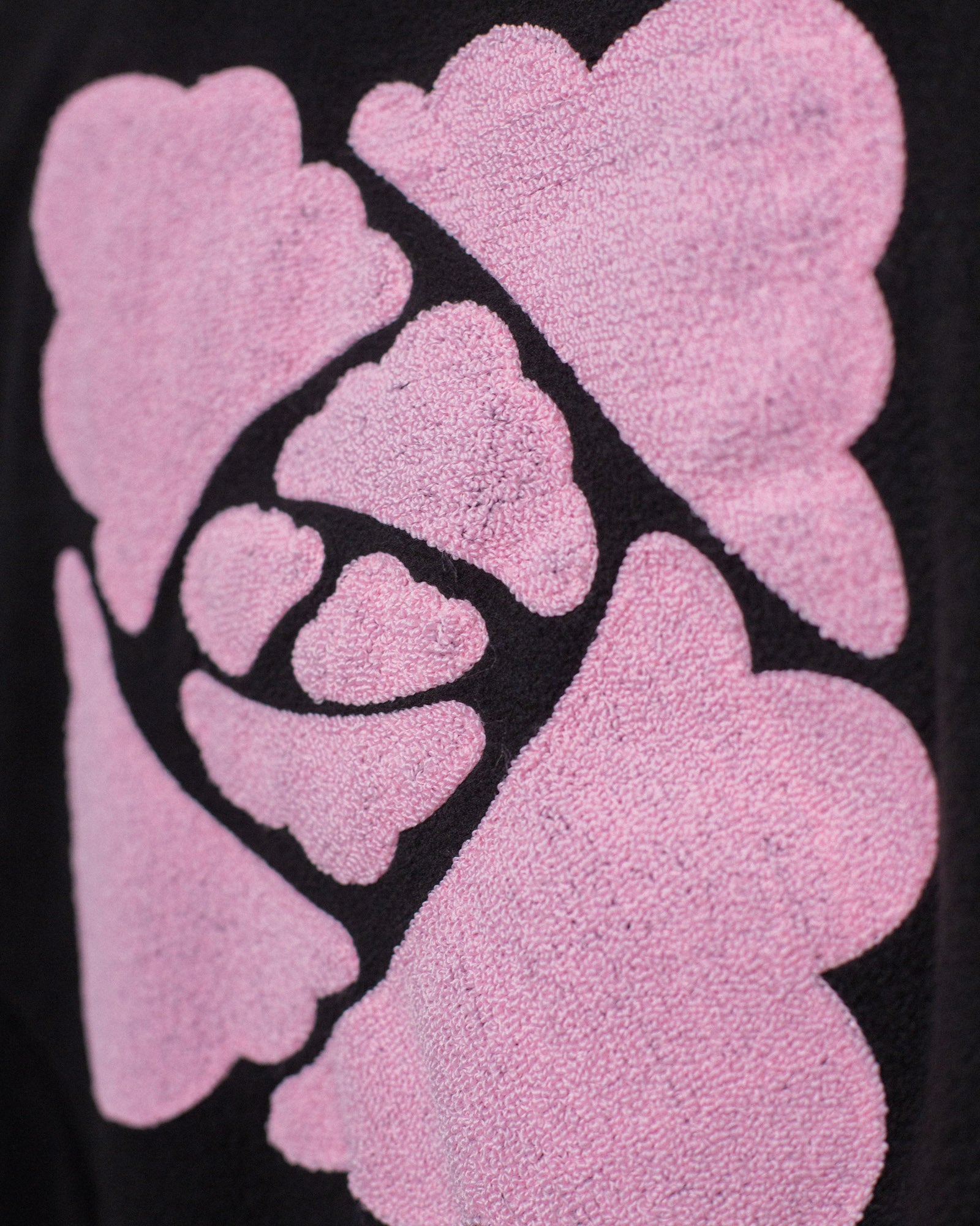 Detaillierte Nahaufnahme der textilen Struktur des rosa Rückenprints mit Wolkenlinien auf schwarzem Stoff.