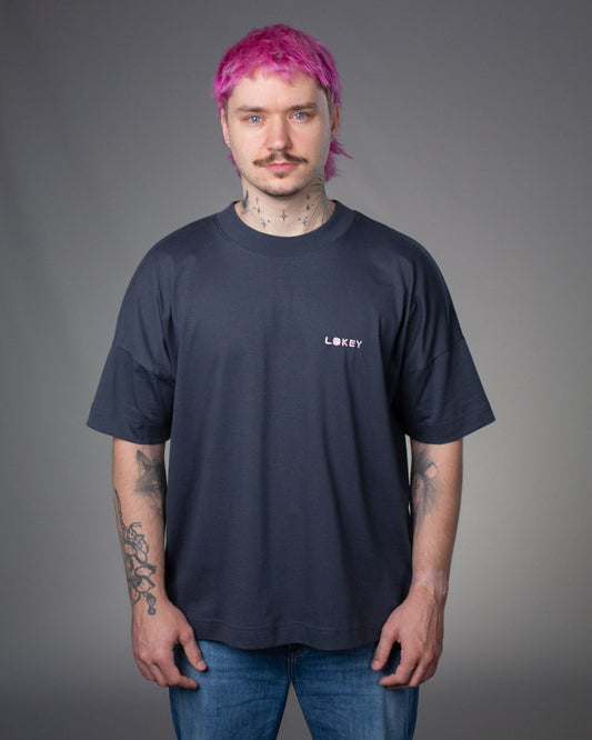 	Frontansicht des dunkelblauen T-Shirts. Der gestickte Schriftzug „LOKEY“ ist links auf Brusthöhe in Rosa aufgebracht, das „O“ besteht aus einem stilisierten Blumenornament.