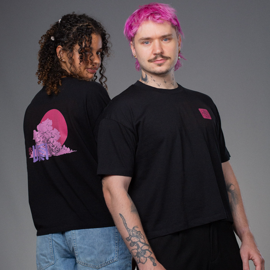 Zwei Personen stehen Rücken an Rücken und tragen das gleiche schwarze T-Shirt mit pinkem Front- und Rückendruck. Der Rückendruck zeigt eine große Wolke mit pinker Sonne und lilafarbenem „LOKEY“-Schriftzug, der Frontprint ein rechteckiges Blumenlogo in Pink.